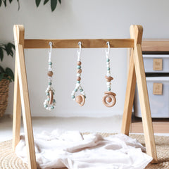 3 handmade silicone and wood baby activity gym toys in gender neutral sage hanging from a kmart wooden play gym frame