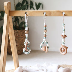 Close up of 3 handmade silicone and wood baby activity gym toys in gender neutral sage hanging from a kmart wooden play gym frame