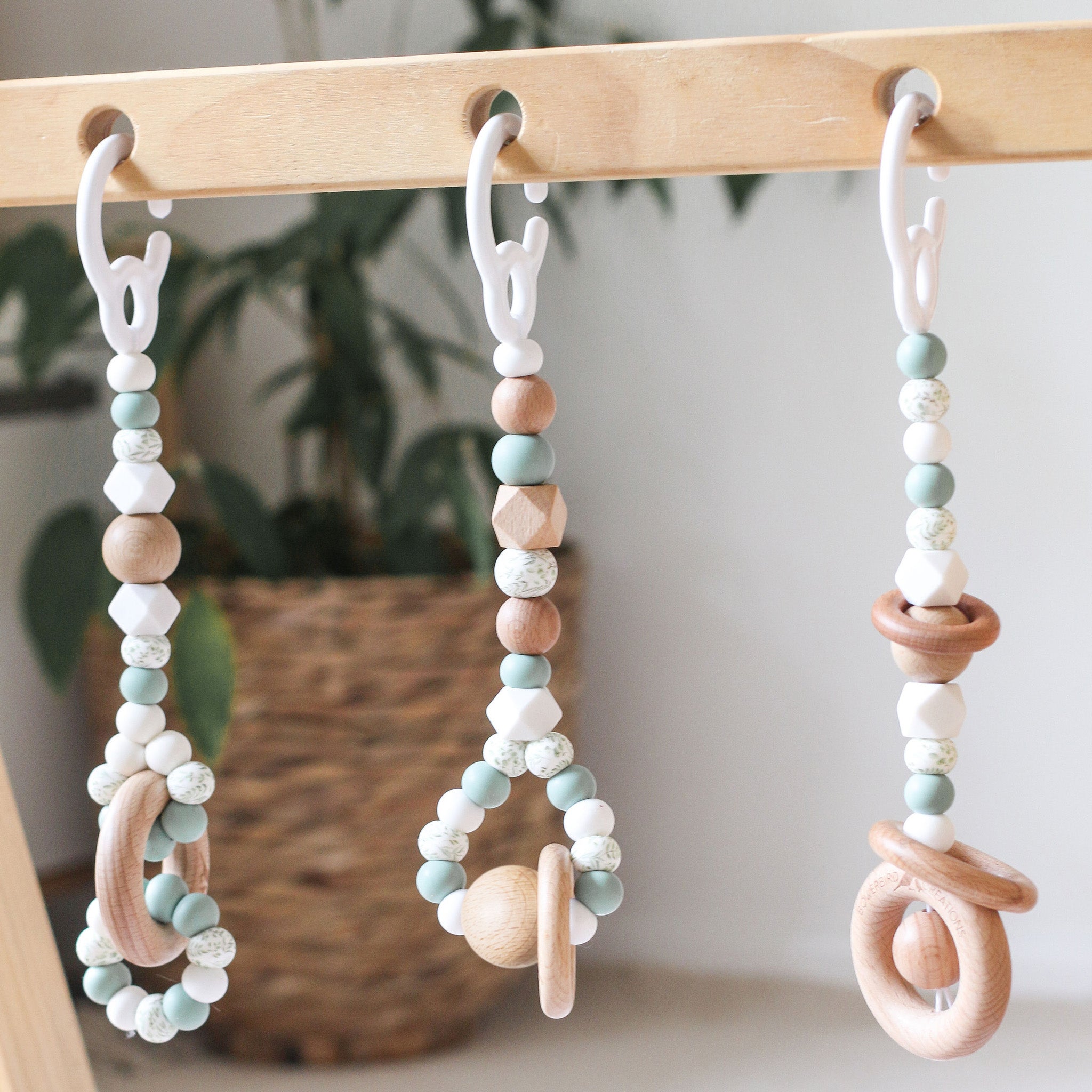 Close up of 3 gender neutral sage handmade silicone and wood baby activity gym toys in hanging from a kmart wooden play gym frame