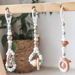 Close up of 3 gender neutral sage handmade silicone and wood baby activity gym toys in hanging from a kmart wooden play gym frame