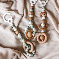 Close up of 3 handmade silicone and wood baby activity gym toys in gender neutral sage