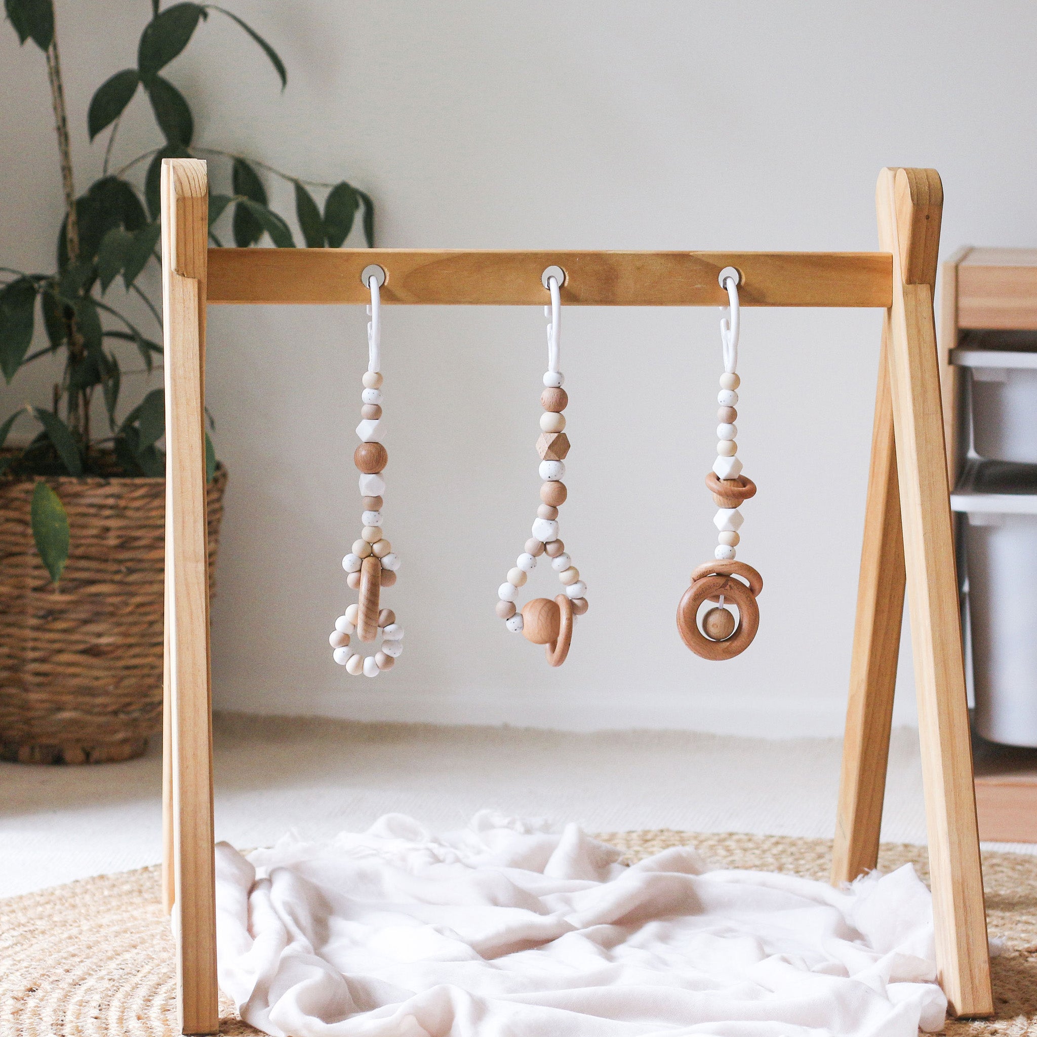 3 handmade silicone and wood baby play gym toys in beige hanging on the Kmart wooden activity gym frame