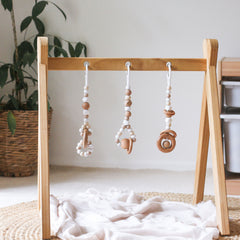 3 handmade silicone and wood baby play gym toys in beige hanging on the Kmart wooden activity gym frame
