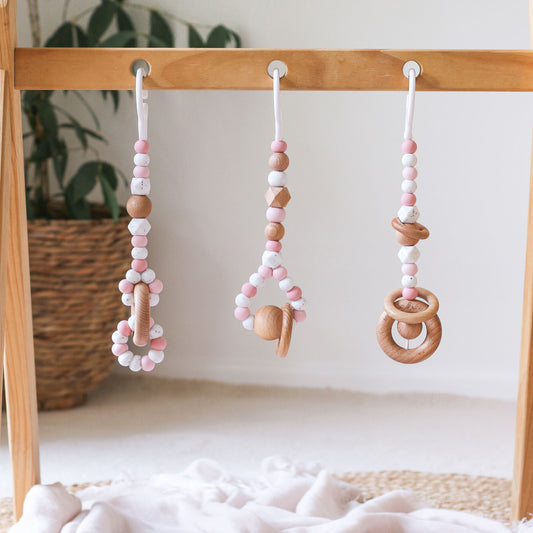 Close up of 3 pink baby play gym toy made from silicone and wood hanging from a kmart wooden activity gym frame