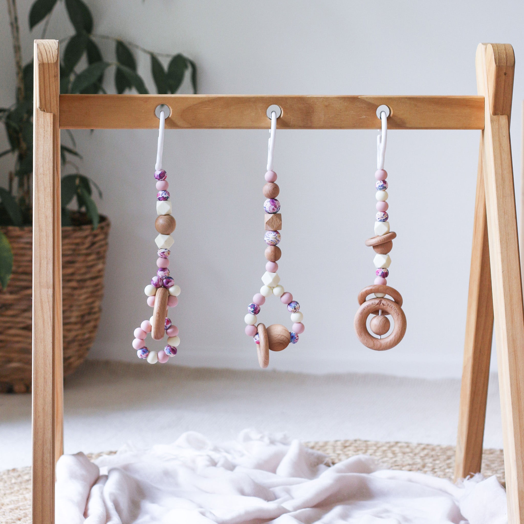 3 handmade silicone and wood baby play gym toys in pink, cream and floral hanging on the Kmart wooden activity gym frame