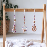 3 handmade silicone and wood baby play gym toys in pink, cream and floral hanging on the Kmart wooden activity gym frame