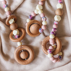 Close up of 3 3 handmade silicone and wood baby play gym toys in pink, cream and floral.