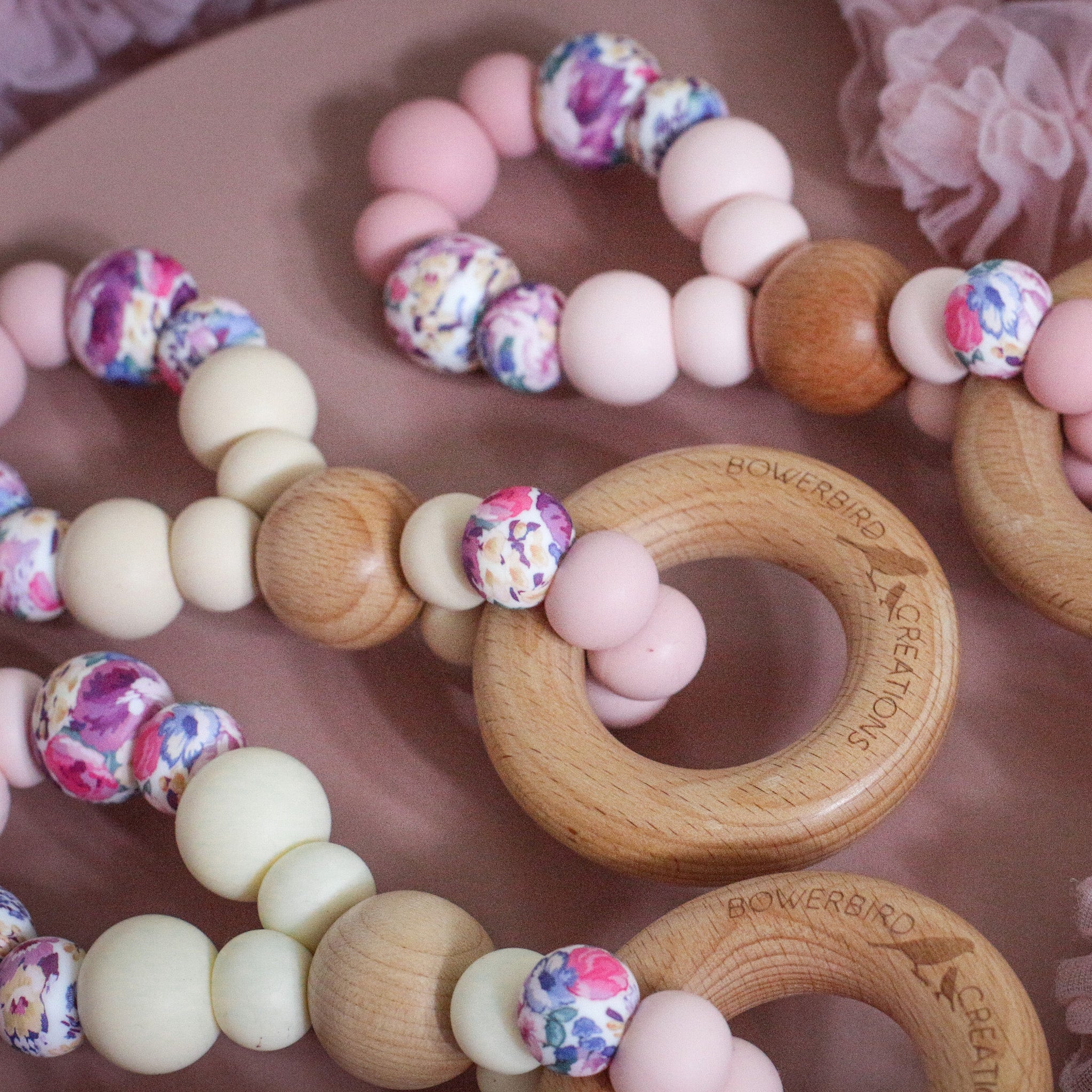 Teething toys handmade from silicone and beech wood by Bowerbird Creations. Made in Australia. Pink, beige, cream and roses. Close up photo.