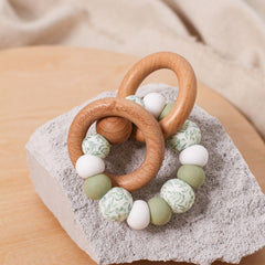 Newborn teether and montessori toys. Handmade from BPA-free silicone and beech wood timber teething rings that rattle when shaken. Lint, white and foliage designs.
