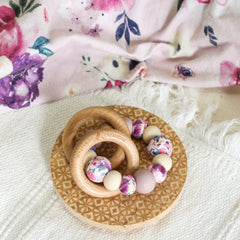 Teething and Montessori toys. Handmade newborn teether with wood teething rings that rattle when shaken. Handmade in Australia from BPA-free silicone and beech wood timber. Dreamer teether by Bowerbird Creations. Purple, mauve, beige and floral.