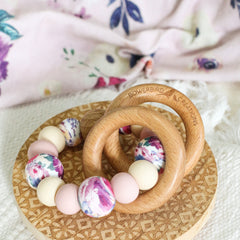 Teething and Montessori toys. Handmade newborn teether with wood teething rings that rattle when shaken. Handmade in Australia from BPA-free silicone and beech wood timber. Dreamer teether by Bowerbird Creations. Pink, beige and floral.