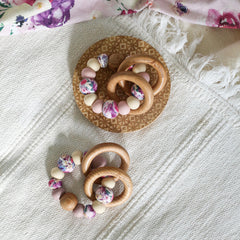 Teething and Montessori toys. Handmade newborn teether with wood teething rings that rattle when shaken. Handmade in Australia from BPA-free silicone and beech wood timber. Dreamer teether by Bowerbird Creations. Pink, purple, mauve, beige and floral.