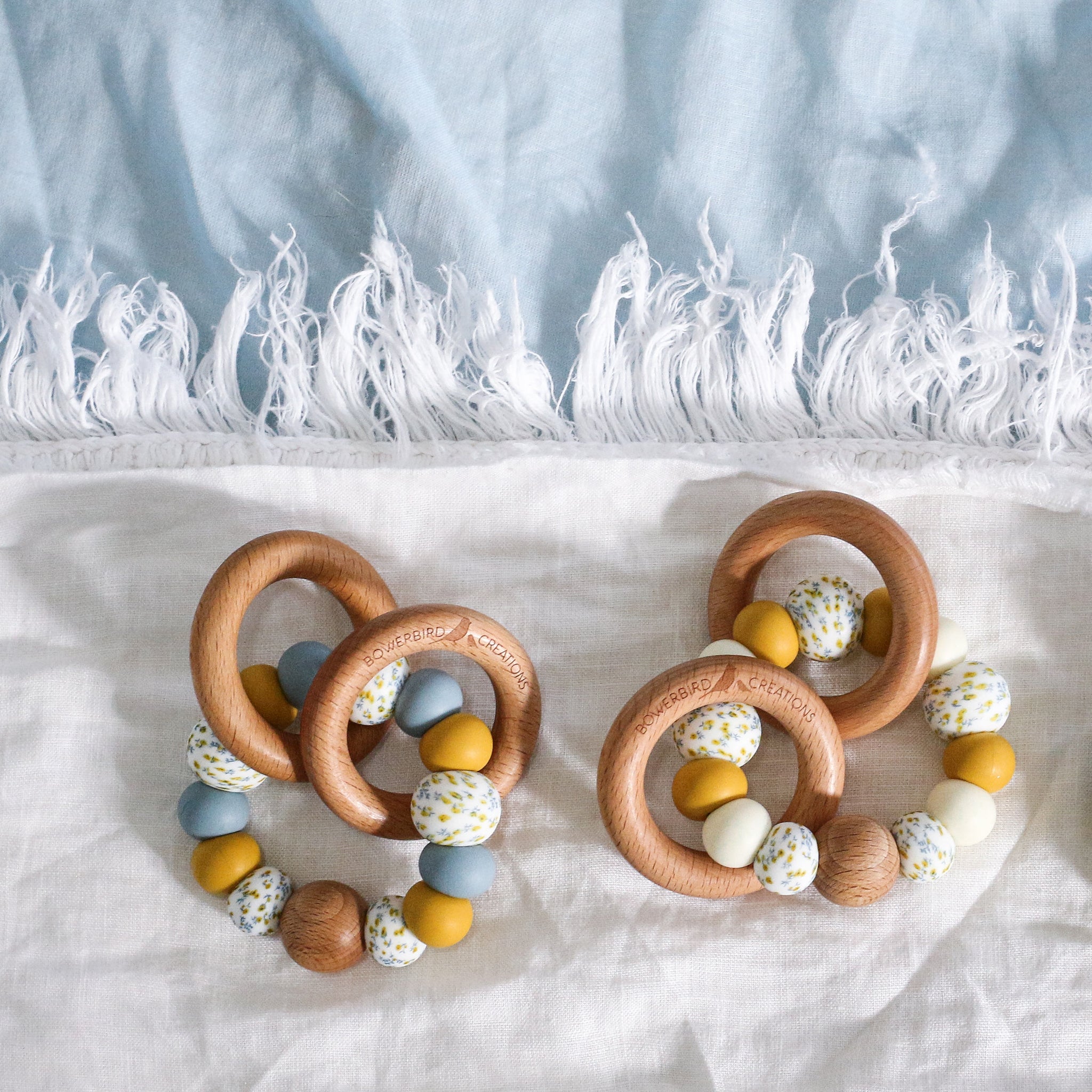 Handmade teething toys made in Australia from silicone beads and beech wood timber teething rings that rattle when shaken. Dreamer Teether by Bowerbird Creations. Blue mustard, cream and Wattle.
