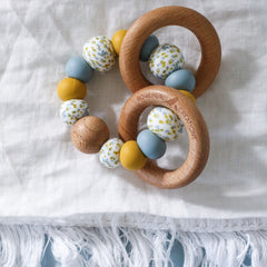Handmade teething toys made in Australia from silicone beads and beech wood timber teething rings that rattle when shaken. Dreamer Teether by Bowerbird Creations. Blue mustard and Wattle.