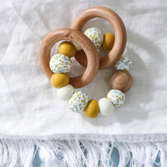 Handmade teething toys made in Australia from silicone beads and beech wood timber teething rings that rattle when shaken. Dreamer Teether by Bowerbird Creations. Mustard, cream and Wattle.
