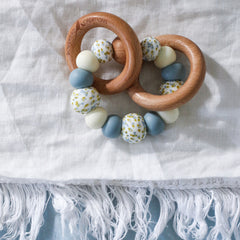 Handmade teething toys made in Australia from silicone beads and beech wood timber teething rings that rattle when shaken. Dreamer Teether by Bowerbird Creations. Blue, cream and Wattle.