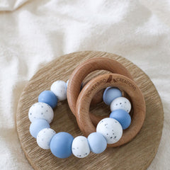 Dreamer teething ring for infants. Made with a ring of silicone beads and 2 timber teething rings that rattle when shaken. Handmade. Made in Australia. Non-toxic and safe. Blue and granite.