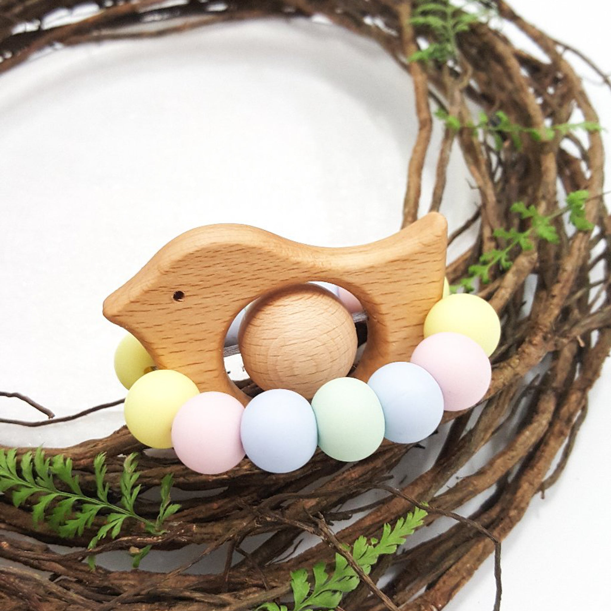 Newborn teether and Montessori toys. Handmade bird shaped teether made with BPA-free silicone and beech wood timber teething ring. Made in Australia by Bowerbird Creations. Tweet teether in pastel rainbow.