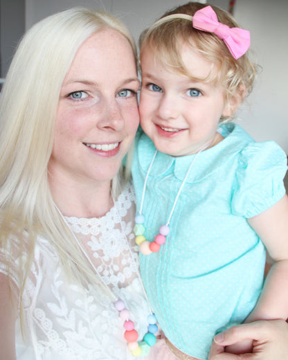 Mum and daughter in matching pastel rainbow silicone necklaces.
