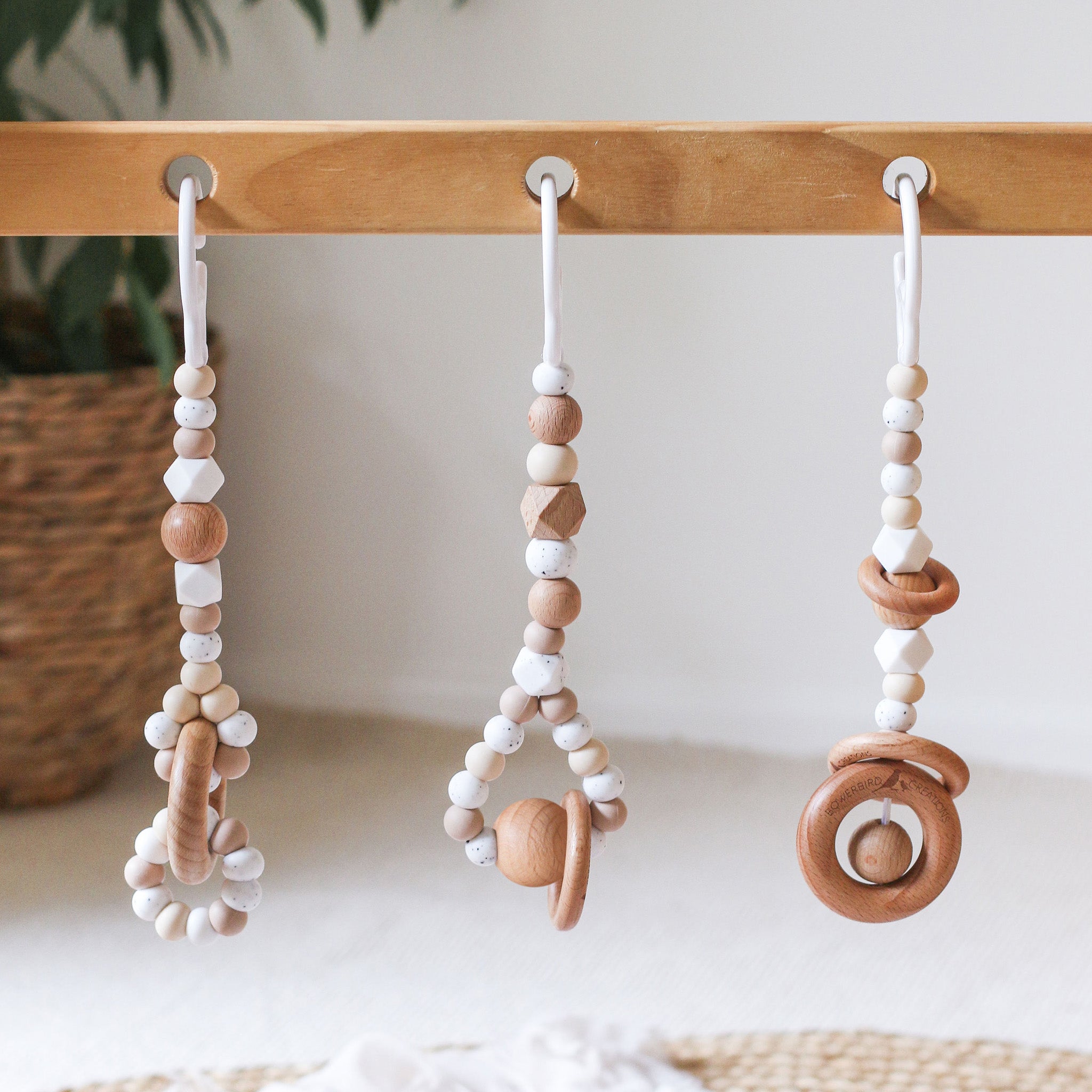 Close up of 3 handmade silicone and wood baby play gym toys in beige hanging on the Kmart wooden activity gym frame 