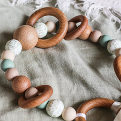 Close up of handmade silicone and wood pram toy in sage, beige and printed leafy beads
