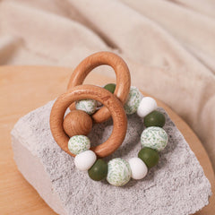 Newborn teether and montessori toys. Handmade from BPA-free silicone and beech wood timber teething rings that rattle when shaken. Olive, white and foliage designs. 