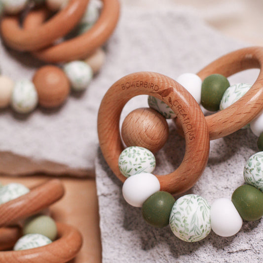 Newborn teether and montessori toys. Handmade from BPA-free silicone and beech wood timber teething rings that rattle when shaken. Olive, white and foliage designs. 