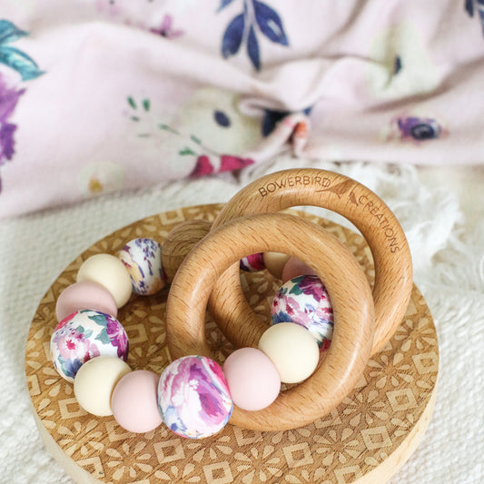 Teething and Montessori toys. Handmade newborn teether with wood teething rings that rattle when shaken. Handmade in Australia from BPA-free silicone and beech wood timber. Dreamer teether by Bowerbird Creations. Pink, beige and floral. 