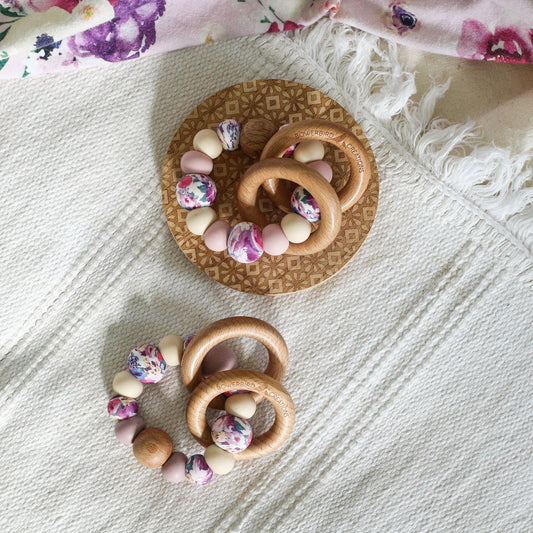 Teething and Montessori toys. Handmade newborn teether with wood teething rings that rattle when shaken. Handmade in Australia from BPA-free silicone and beech wood timber. Dreamer teether by Bowerbird Creations. Pink, purple, mauve, beige and floral. 
