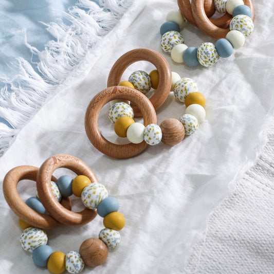 Handmade teething toys made in Australia from silicone beads and beech wood timber teething rings that rattle when shaken. Dreamer Teether by Bowerbird Creations. Blue mustard, cream and Wattle. 