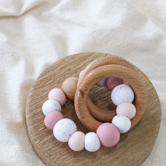 Dreamer teething ring for infants. Made with a ring of silicone beads and 2 timber teething rings that rattle when shaken. Handmade. Made in Australia. Non-toxic and safe. Pink and granite. 