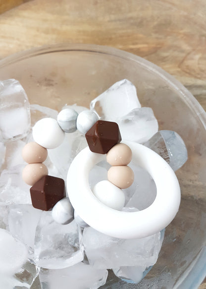 Baby teething toy handmade from silicone sitting in a bowl of ice. Brown, beige, marble, white.