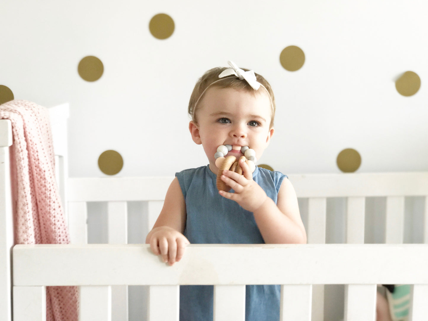 Baby chewing on a silicone teething toy with 3 wooden rings. Pink, white, marble.